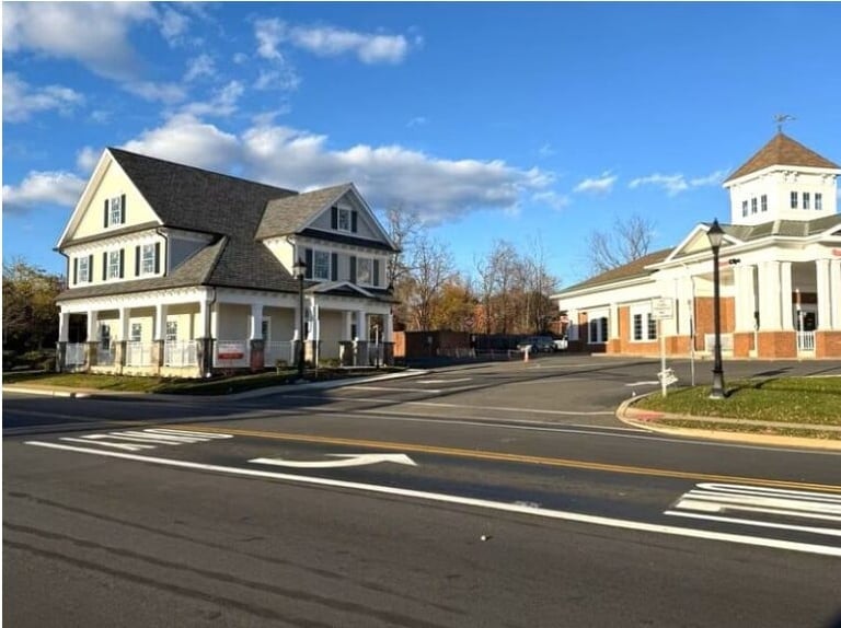 Two historic buildings on a tree-lined street with clear blue sky and white road markings.